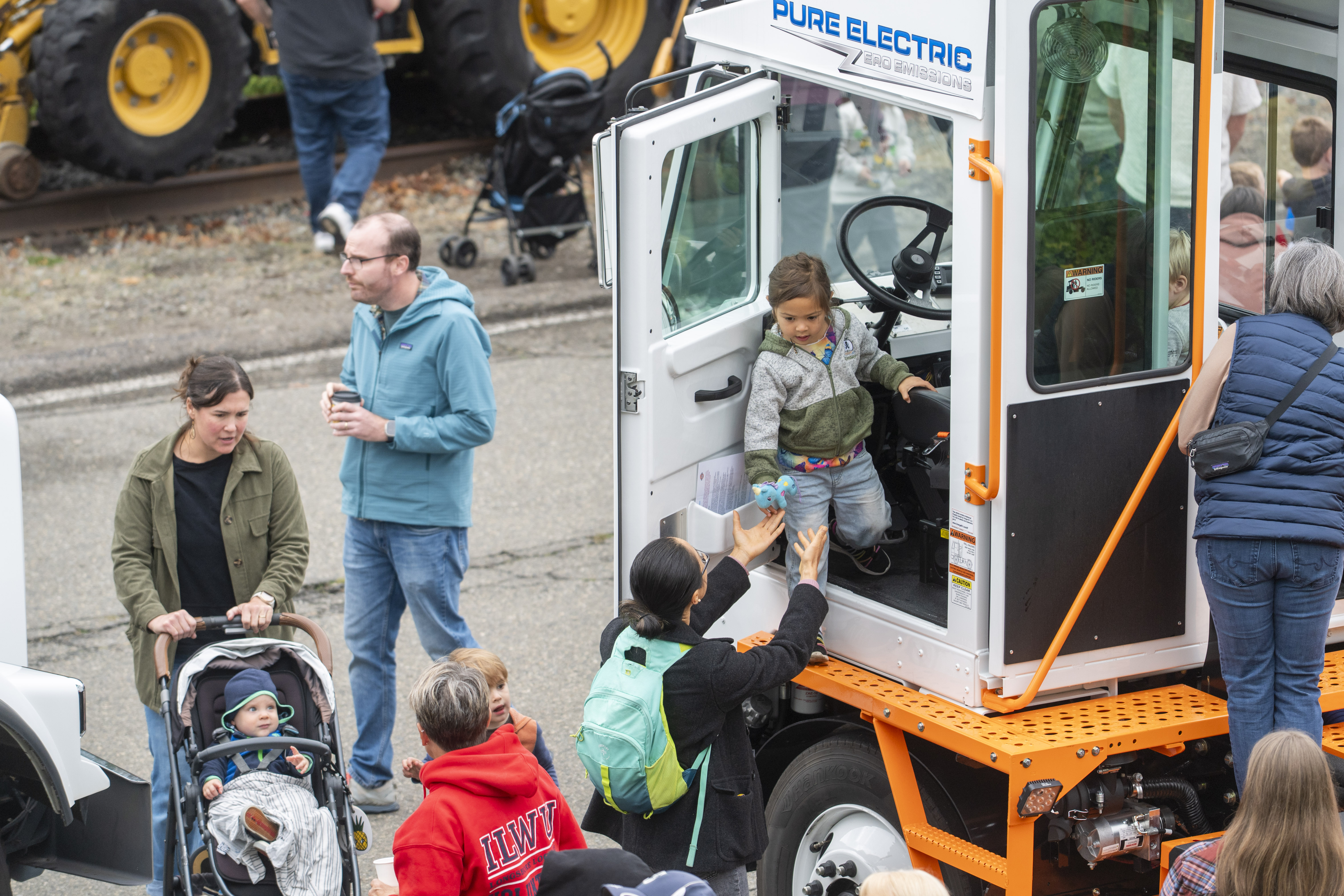 A man lifts his child out of a construction vehicle while other people around look on.