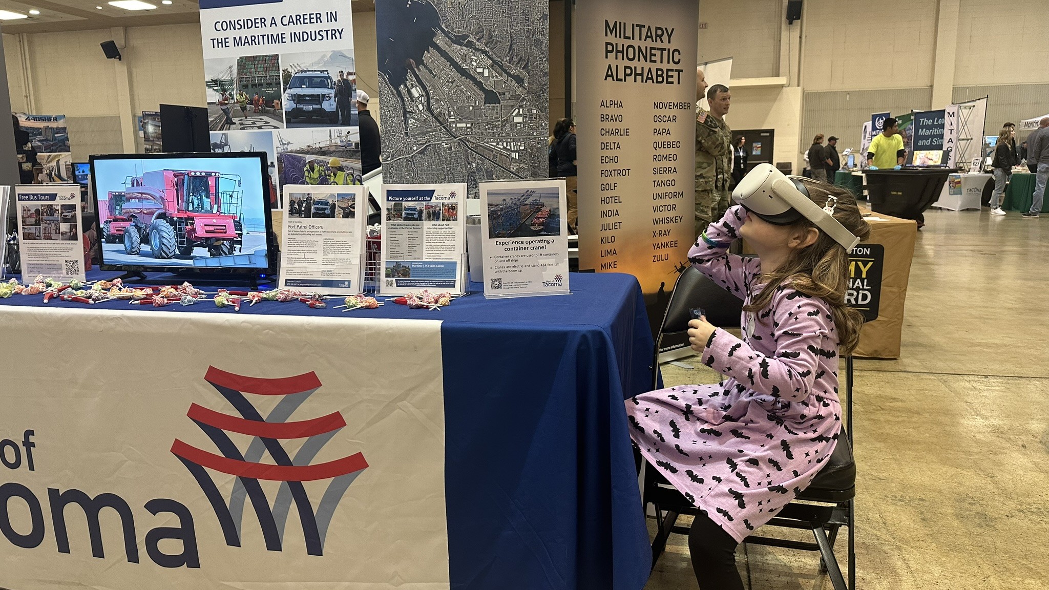 A girl in a purple dress sits in front of a Port booth while wearing a VR headset.