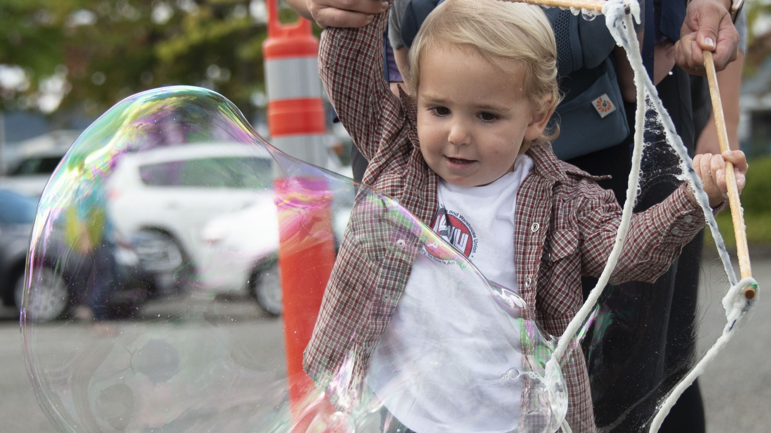 A toddler playing with large bubbles while their parent helps them.