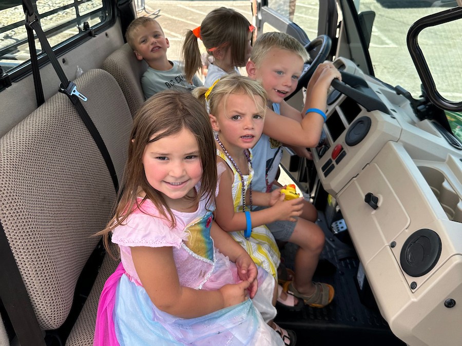 A group of children smile while sitting the cab of a John Deere tractor. 