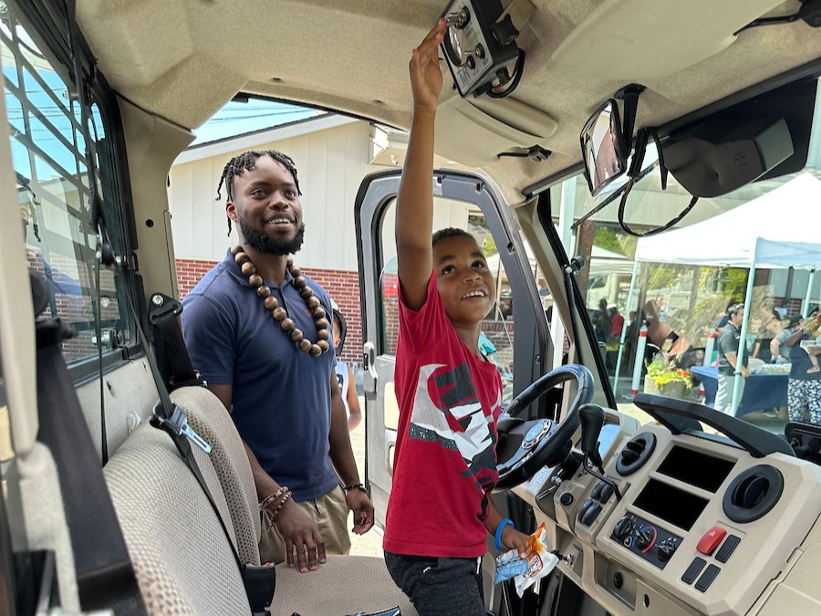A young boy and his caregiver smile while looking at the controls in a large truck.