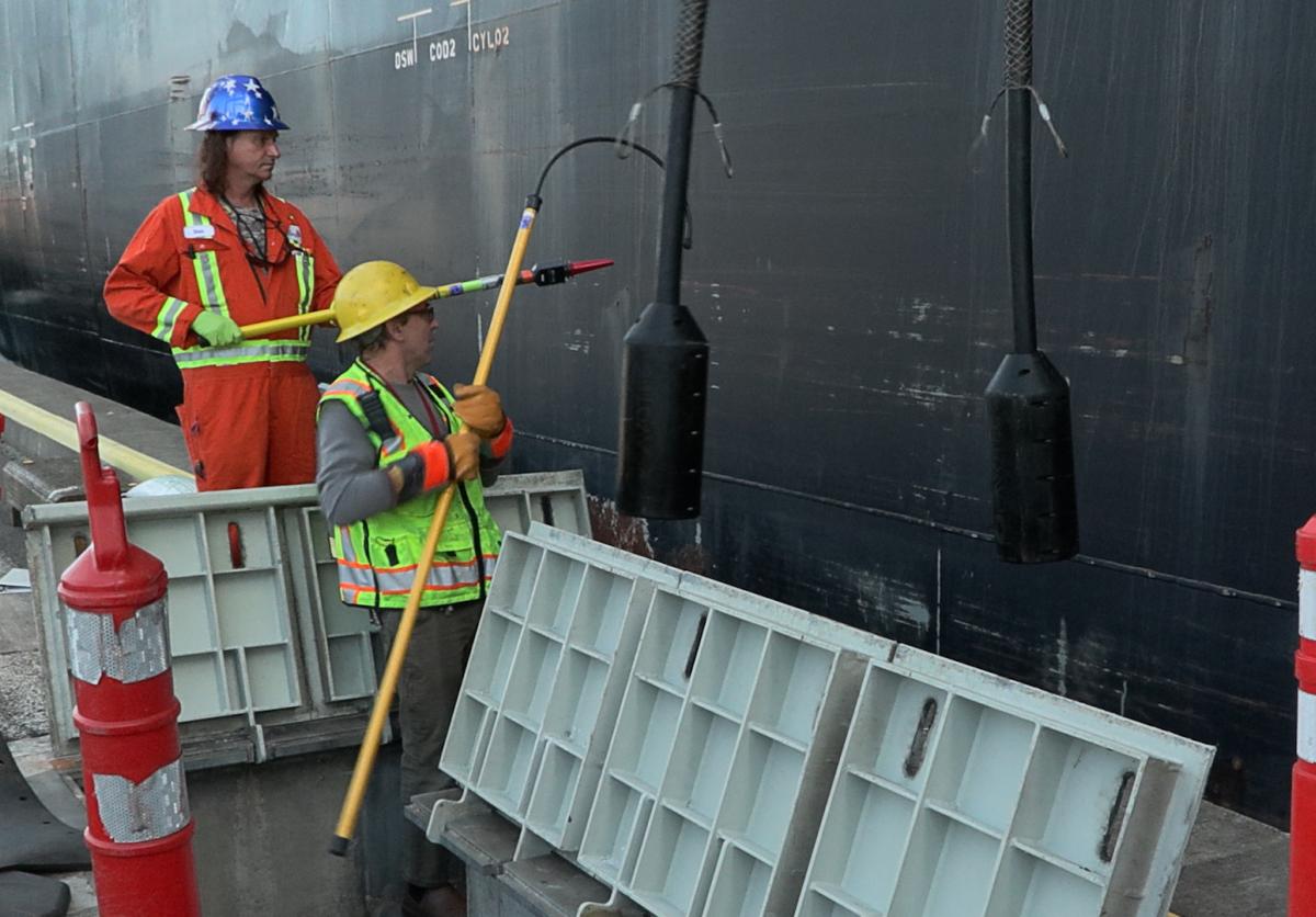 Two men in safety equipment pulling electrical cords down from a vessel.